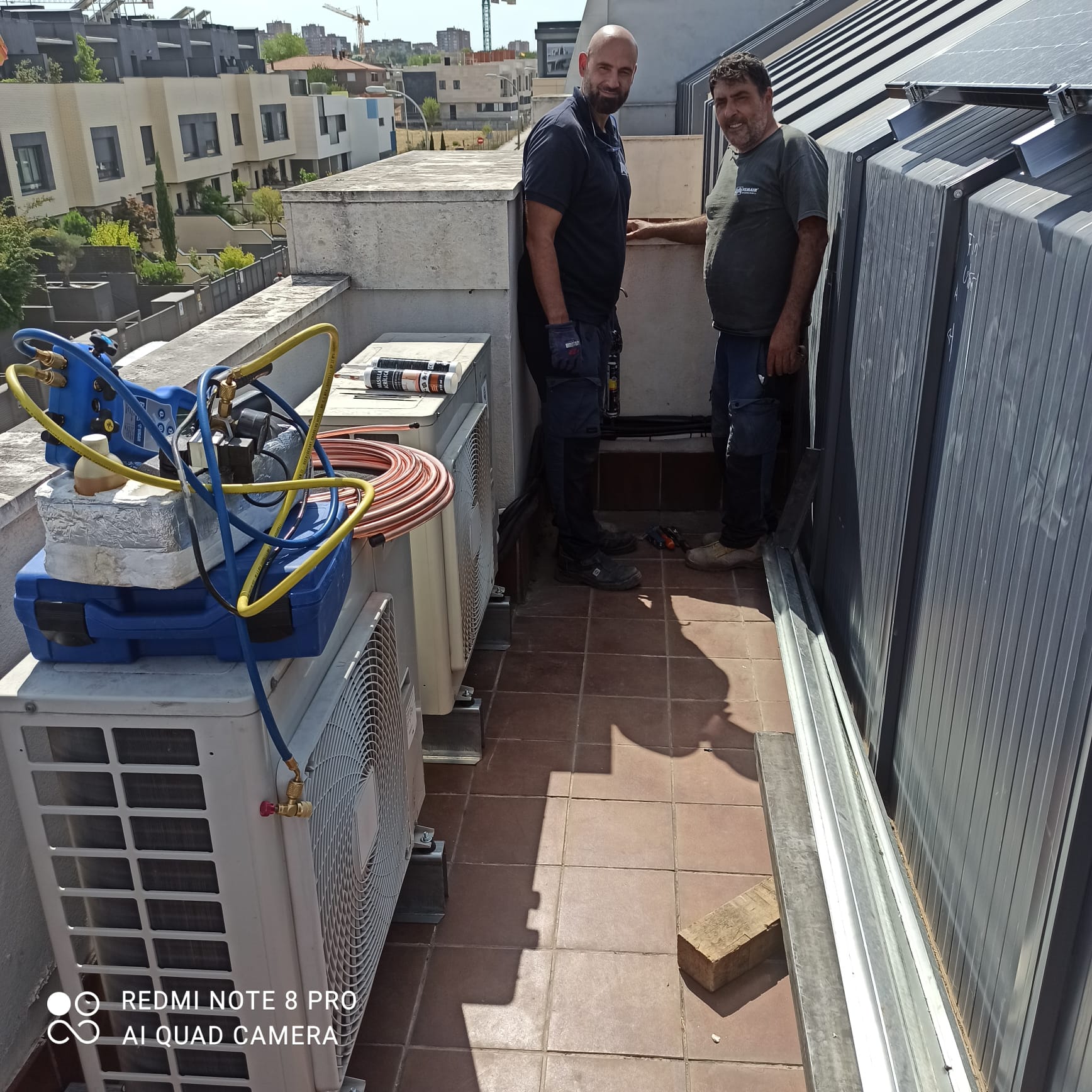 Dos técnicos junto a unidades exteriores de aire acondicionado y equipo de medición en una terraza.