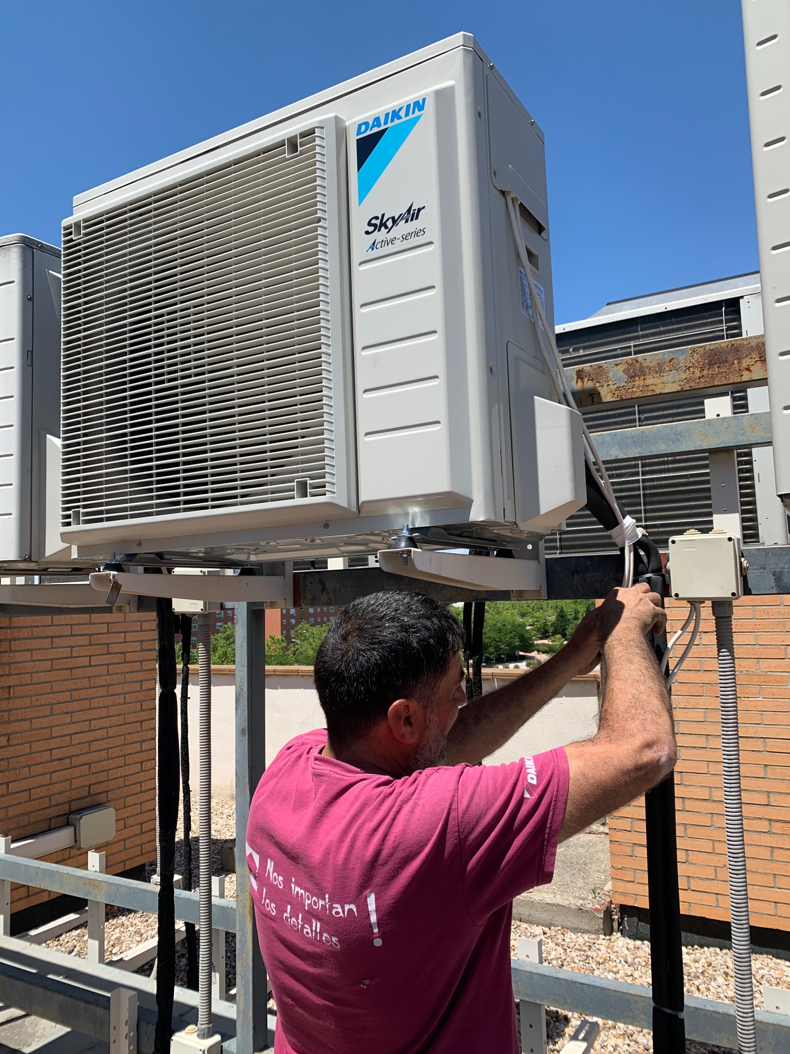 Técnico trabajando junto a una unidad exterior de aire acondicionado montada sobre soportes metálicos.